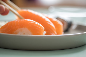 Woman eating Japanese salmon Nigiri and Maki Sushi with wooden chopsticks from porcelain plate