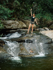Fototapeta na wymiar Beautiful red-haired sexy young woman model in a T-shirt and shorts in the jungle, stream water in mountain of waterfall in deep forest in Thailand.