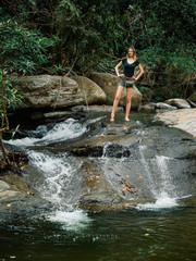 Beautiful red-haired sexy young woman model in a T-shirt and shorts in the jungle, stream water in mountain of waterfall in deep forest in Thailand.