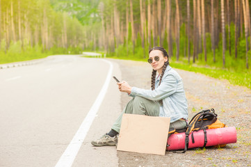 girl hitchhiking sitting on a backpack and  using smartphone
