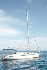 Fototapeta premium Floating yacht with sails down in calm sea. A boat lowered the sails and anchored near the coast