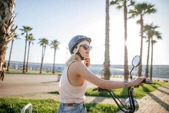 people, transport, technology, travel and vacation concept - outdoor portrait of pretty cute tourist woman smiling beside her electric bike in park with palms in summer morning.