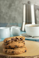 chocolate chip cookies on wooden plank with back ground of coffee cup and coffee pot on wooden table