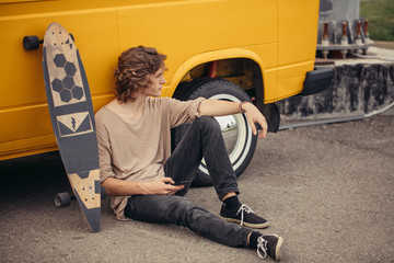 Fototapeta na wymiar Young hipster guy sitting next his yellow car during road trip