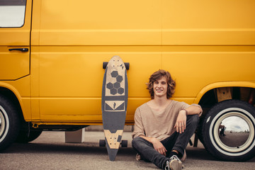 Young hipster guy sitting next his yellow car during road trip