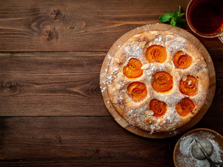 Big Apple pie with apricot, cup of tea, charlotte on dark brown wooden table, top view, copy space