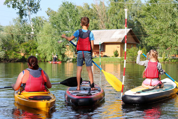 Boy and a girl on paddleboard (SUP) and a girl in kayak. Back view
