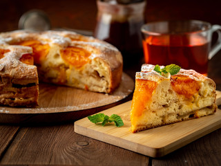 Big Apple pie with apricot and piece, cup of tea, charlotte on dark brown wooden table, side view