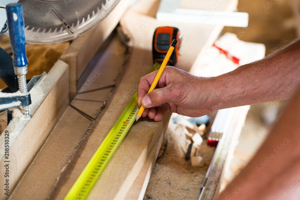 Wall mural Carpenter marking with yellow pencil on the  oak wood board to cut the lenght  in a small wood shop.