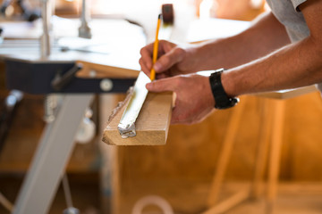 Fototapeta na wymiar Carpenter marking with yellow pencil on the oak wood board in a small wood shop.