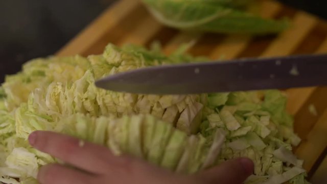 Moving camera and top view of woman's hands slicing savoy cabbage on a wooden cutting board