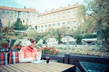 Obraz premium woman sits in an autumn cafe and writes in a notebook. Journalist, writer, freelancer. Mulled wine for a tourist. Woman in a pink jacket and fur headphones 