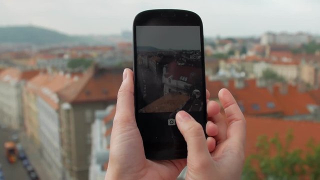 close-up view of female hands holding smartphone and taking photos of red roof buildings in Prague