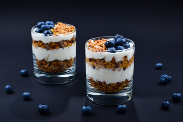 Homemade baked granola with yogurt and blueberries in a glass on a black background. Space for text or design.