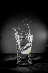 Half Lemon dropped in a glass of water with water splashes with a black to grey background