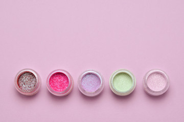Obraz na płótnie Canvas Cosmetics. Makeup. Jars with crumbly bright shadows, glitter. Pink, green, lilac colors on lilac background. Closeup. Space for text or design.