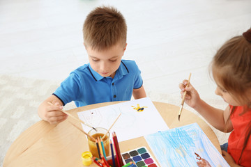 Cute little children painting at table in playing room