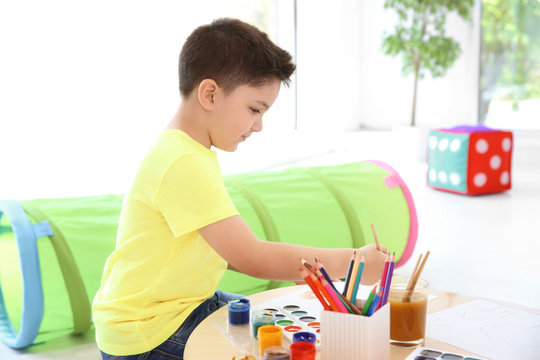 Cute little child painting at table in playing room