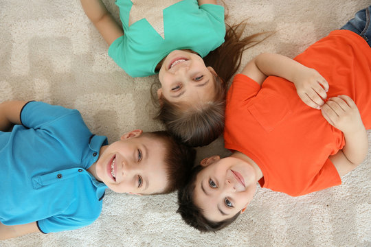 Cute little children lying together on floor in playing room, top view