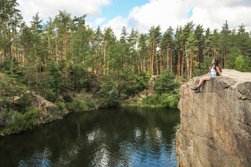 Fototapeta na wymiar Young woman on rock near lake and forest. Camping season