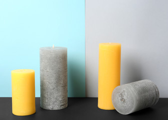 Decorative wax candles on table against color background