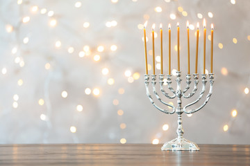 Hanukkah menorah with candles on table against blurred lights © New Africa