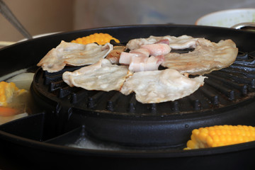 meat, bacon and streaky pork grilled on the black electric grill with corn boil at the side of it.