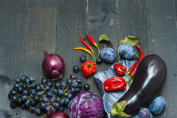 chili peppers, egg plant, grapes, plums on black wood table background