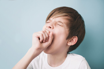 Boy yawns wide with his eyes closed, covering his mouth with his fist