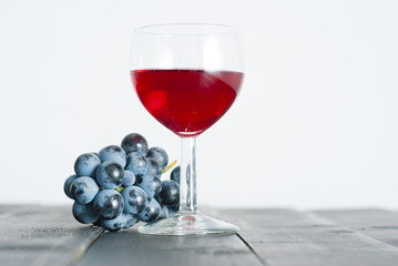 glass of red wine and grapes on black wood table background