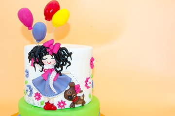 Obraz na płótnie Canvas A Cake With a Dolly with Long Black Hair and Baloons made with Sugar Paste on Orange Background