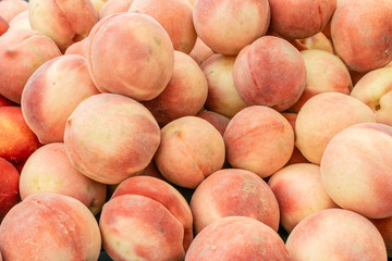 Fresh peaches in pile at outdoor summer market in natural light
