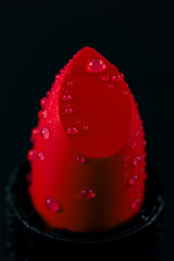 Obraz na płótnie Canvas Women beauty products, luxury fashion and makeup concept with close up of a red lipstick with water droplets, isolated on a dark black background with dramatic lighting