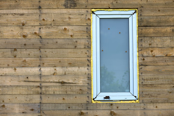 Close-up detail of new narrow plastic vinyl window installed in house wall of natural wooden planks.