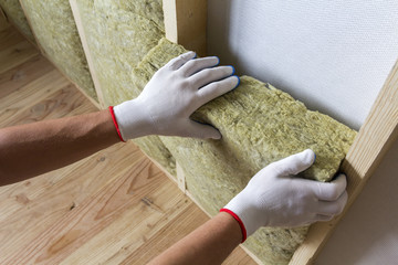 Close-up of worker hands in white gloves insulating rock wool insulation staff in wooden frame for...