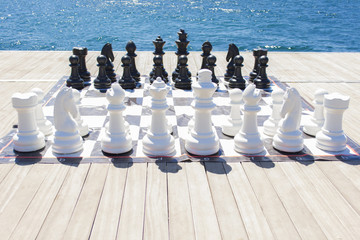 chess game pieces on a board with a blue beach/sea background taken in the day in Istanbul, Turkey.