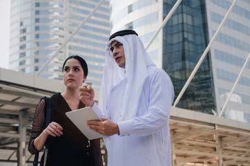 young handsome Arabian business man in white suit holding mobile tablet with secretary asian woman...