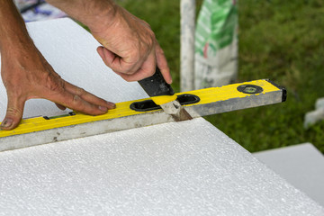 Close-up of worker hand with knife and level cutting white rigid polyurethane foam sheet for house...