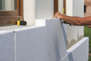 Worker hand with level and knife measuring and cutting white rigid polyurethane foam sheet on wall...