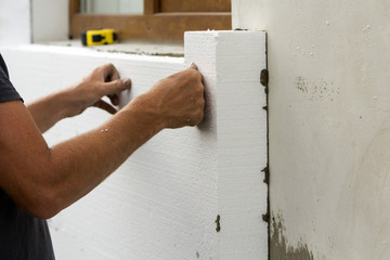 Worker hands installing white rigid polyurethane foam sheet on plastered brick wall. Modern...