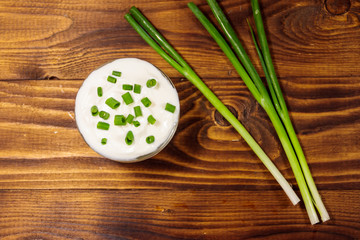 Sour cream and green onion on wooden table. Top view