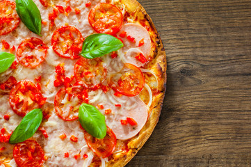Pizza with Mozzarella cheese, Ham, Tomatoes, pepper, Spices and Fresh Basil. Italian pizza on wooden background. with copy space. top view