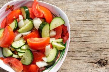Fresh vegetable salad  with tomatoes, cucumbers, onion and olive oil on wooden table. Top view