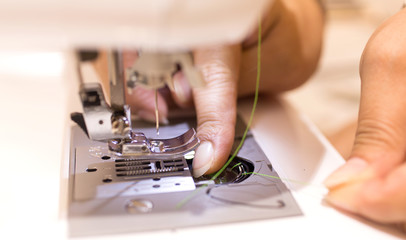 Close up - Female tailor working with sewing machine..Profestional woman hands during sewing work with yarn on sewing machine. Woman fingers are threaded on the sewing machine.