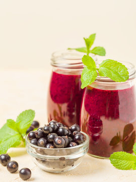 Currant smoothie decorated with fresh green mint leaves and raw ripe berries on yellow pastel background.
