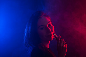 Portrait of young woman in neon red and blue smoke with vape or e-cigarettes