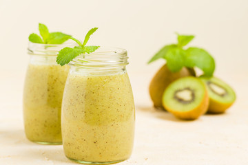 Kiwi smoothie decorated with fresh green mint leaves and raw ripe cut fruit on yellow pastel background.