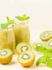 Fototapeta premium Kiwi smoothie decorated with fresh green mint leaves and raw ripe cut fruit on yellow pastel background.