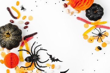 Halloween holiday frame with colorful candy, bats, spiders, pumpkins and decoration on white background. Flat lay. View from above