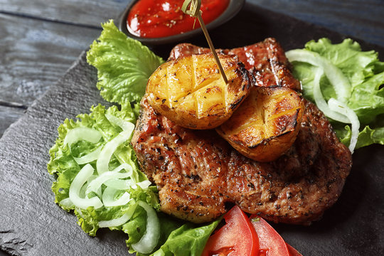 Tasty grilled meat and potatoes served on slate plate, closeup